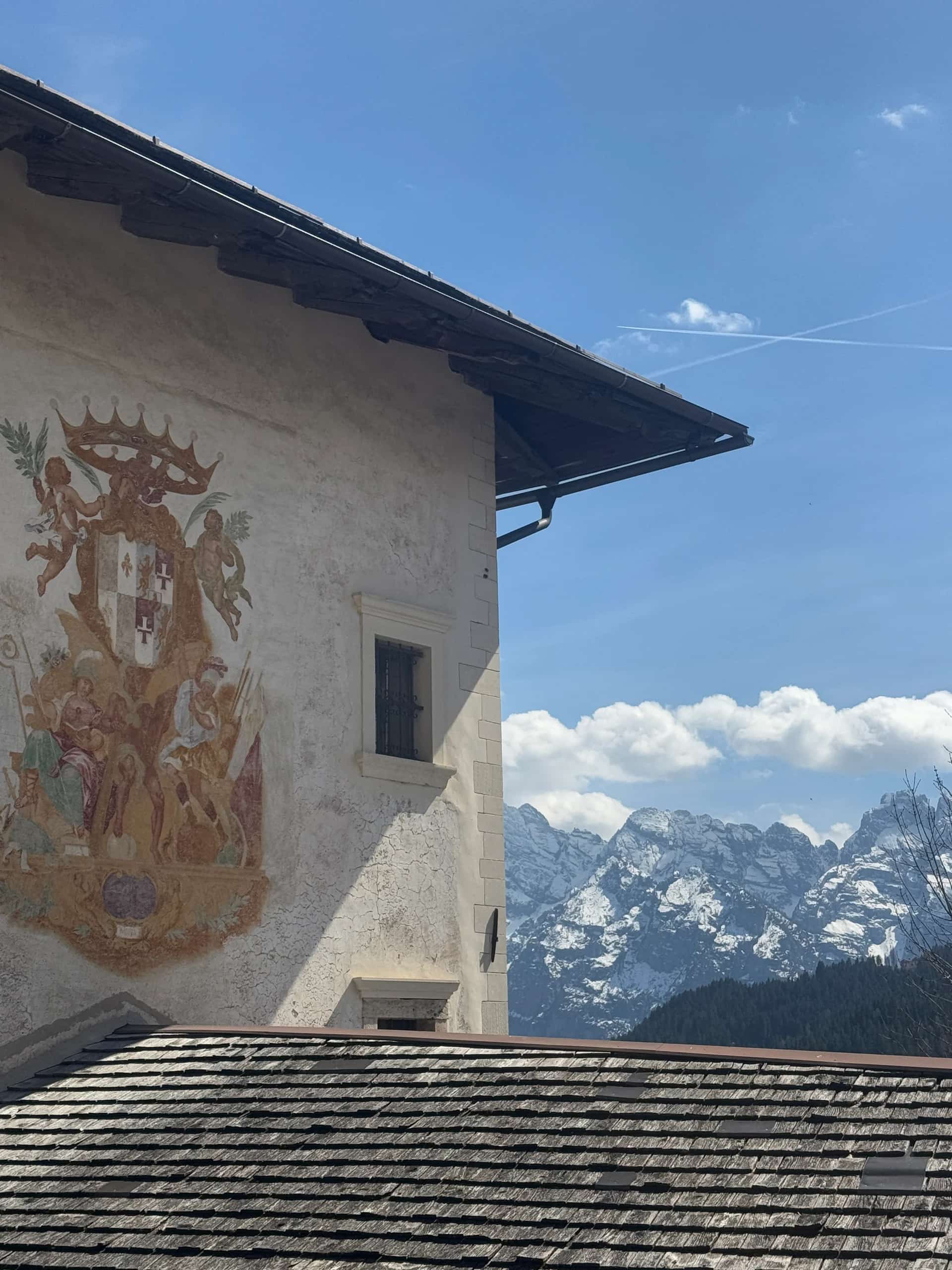 A hand-painted heraldic fresco on the wall of a historic mountain house, the Dolomites rising behind