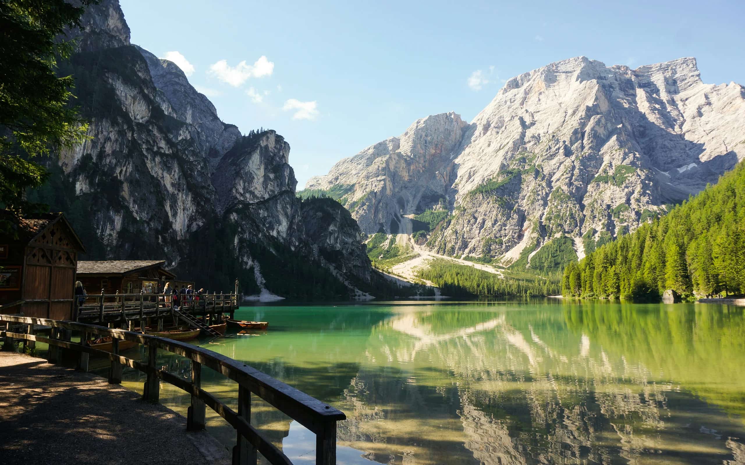 A turquoise alpine lake beneath the Dolomites in summer, a wooden boathouse on the shore